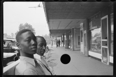 1019__Two African -Americans seated in street with shops