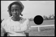 1136_Young black-American young lady with hat ,  in front low rail,  possibly racecourse
