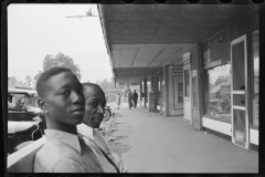 1019__Two African -Americans seated in street with shops