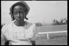 1136_Young black-American young lady with hat ,  in front low rail,  possibly racecourse